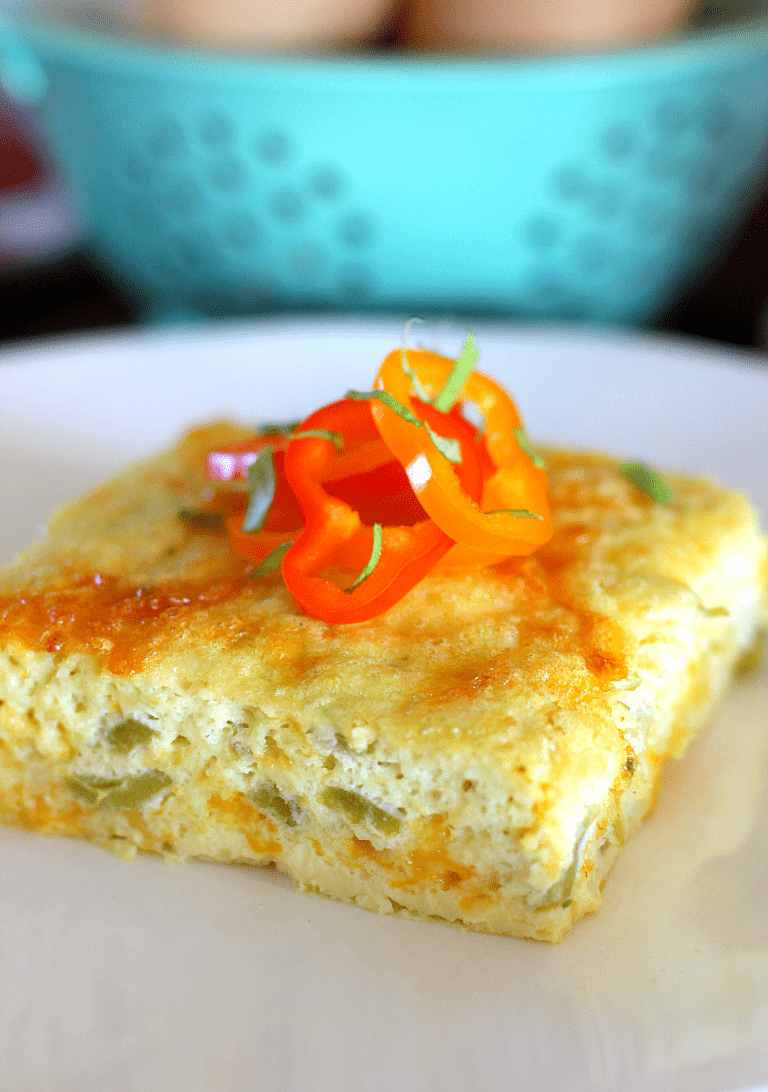 Egg bake slice with shredded cheese and green chiles topped with sliced mini bell peppers.