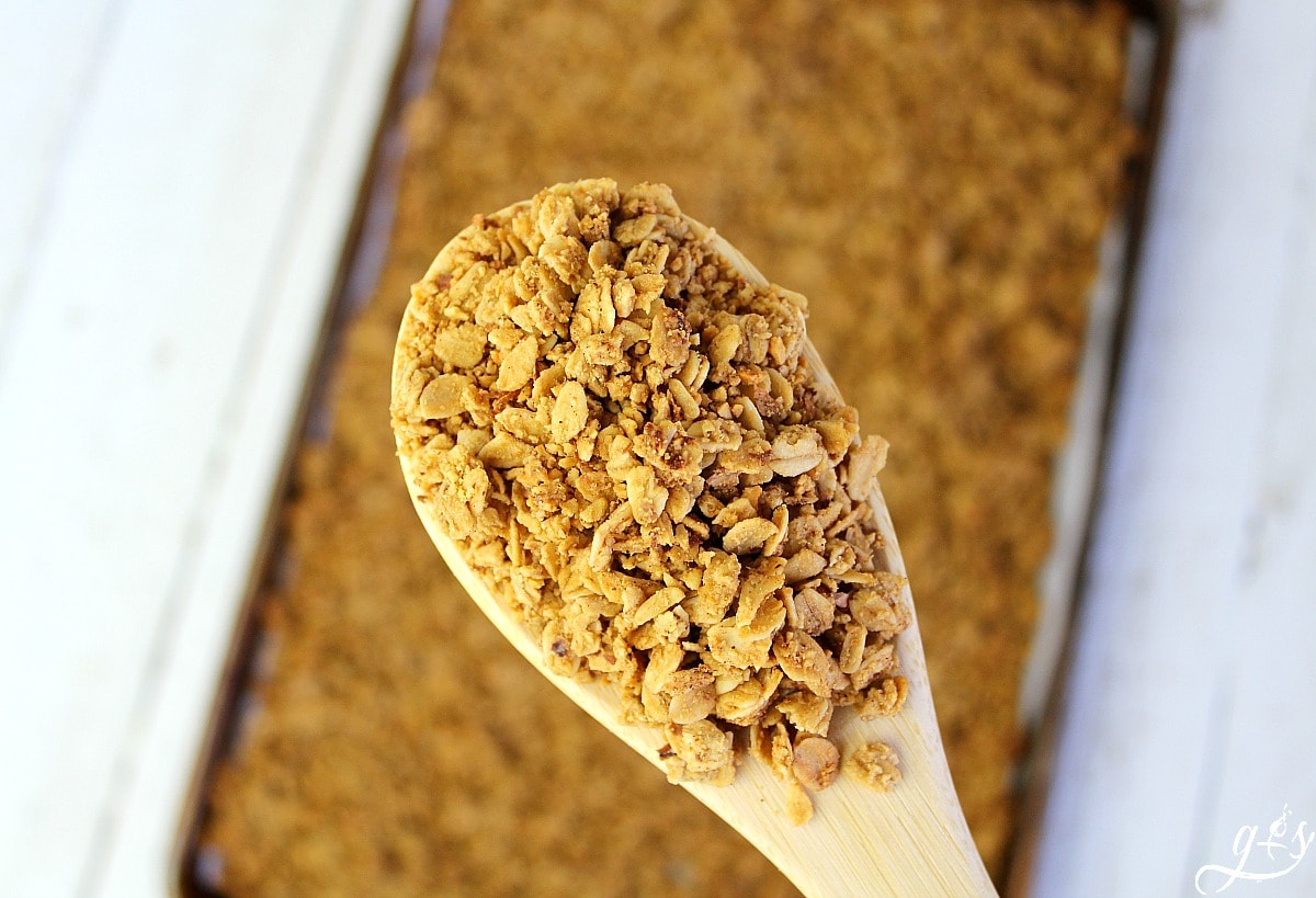 Wooden spoon full of French Toast Granola held over the pan of warm granola. 