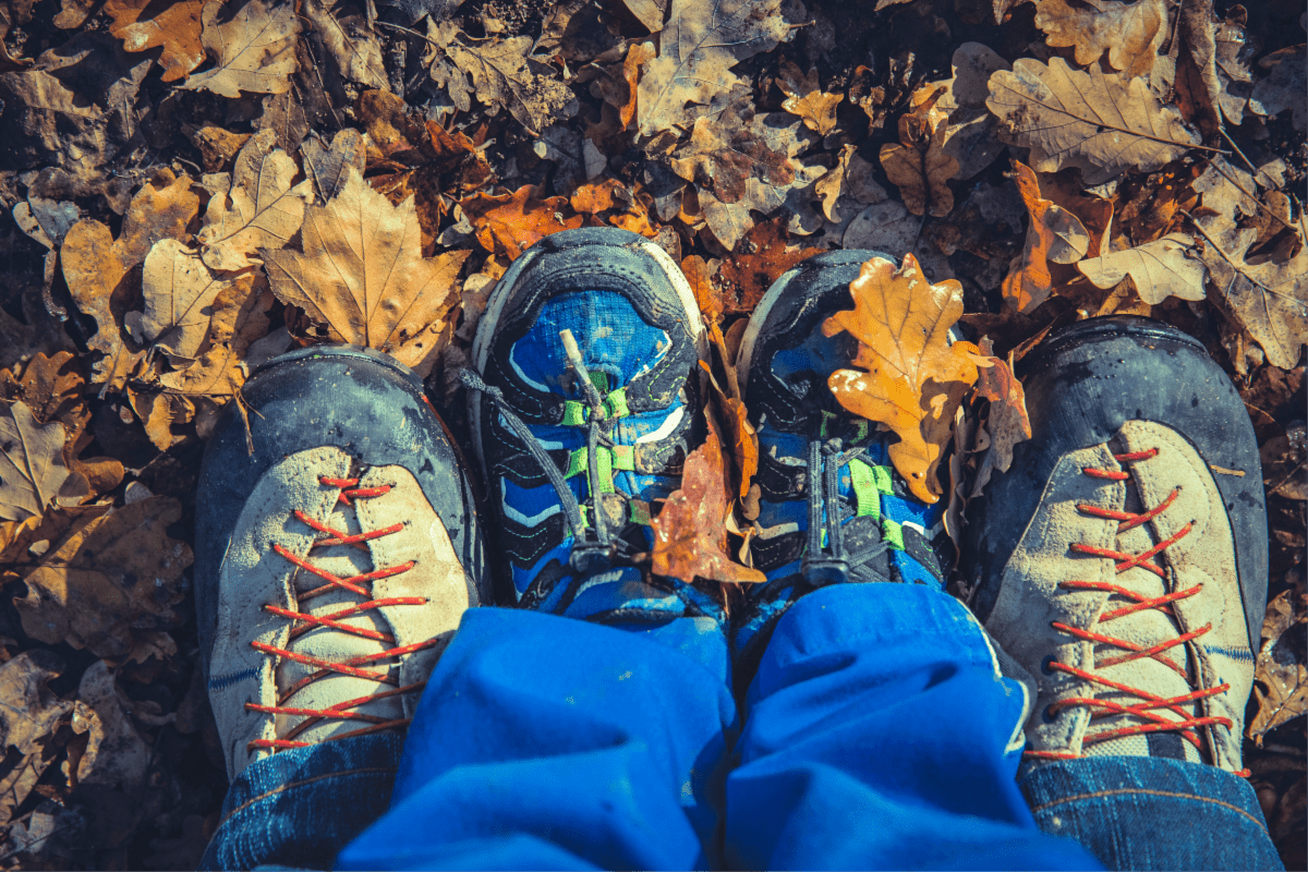 A daddy's feet with his son in between his standing in fall leaves.