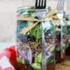 A Greek mason jar salad with quinoa and Kalamata olives with a fork attached.