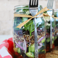 A Greek mason jar salad with quinoa and Kalamata olives with a fork attached.