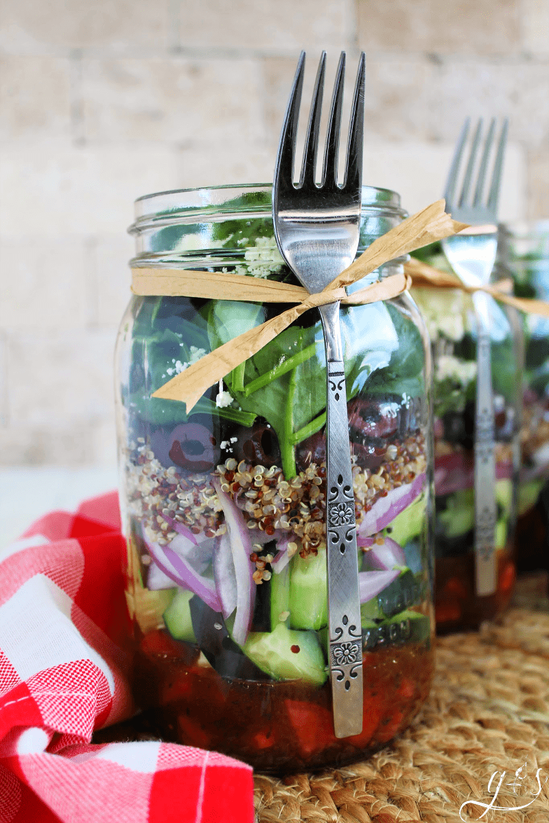 A Greek mason jar salad with quinoa and Kalamata olives with a fork attached.