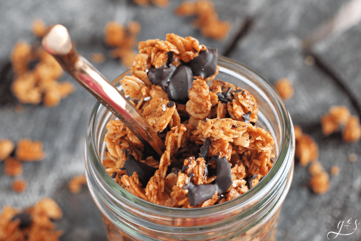 Small clear mason jar full of granola with a bronze spoon submerged in the mixture.