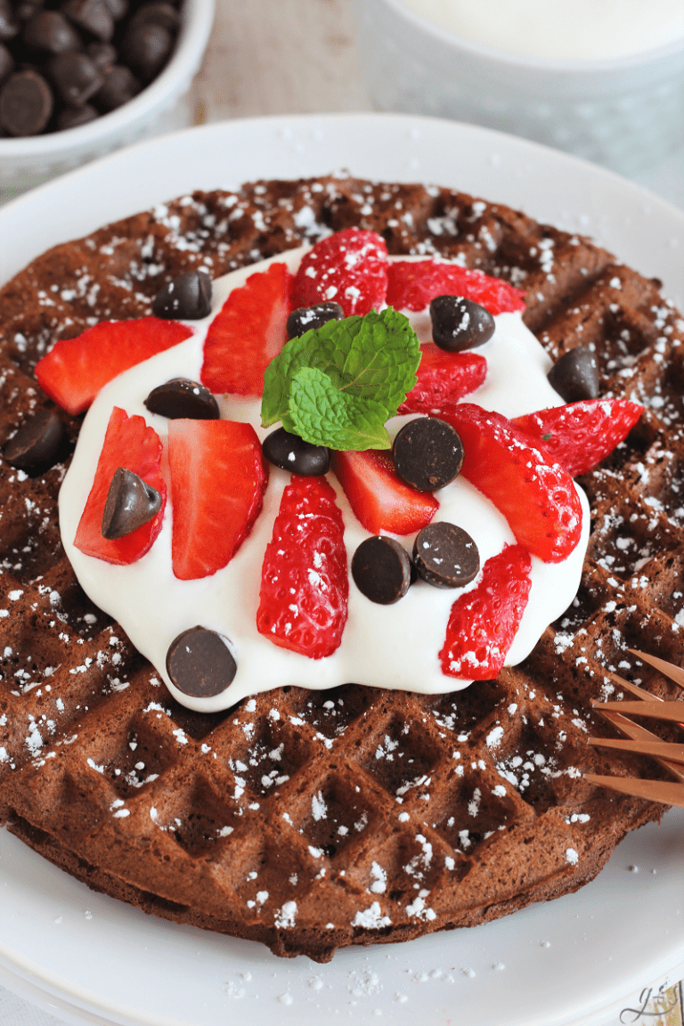 Chocolate chips, sliced strawberries and whipped cream on top of a chocolate waffle.