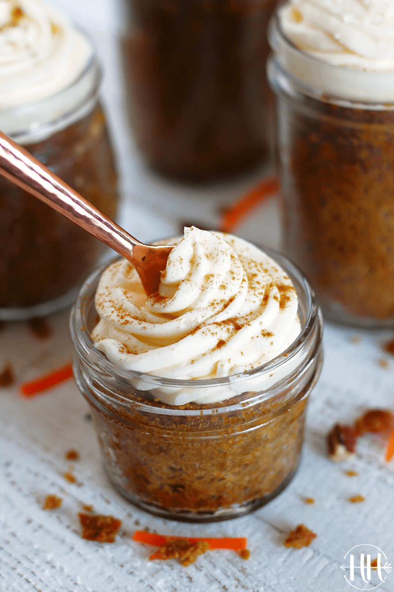 A copper fork digging into a gluten free carrot cake jar topped with frosting.