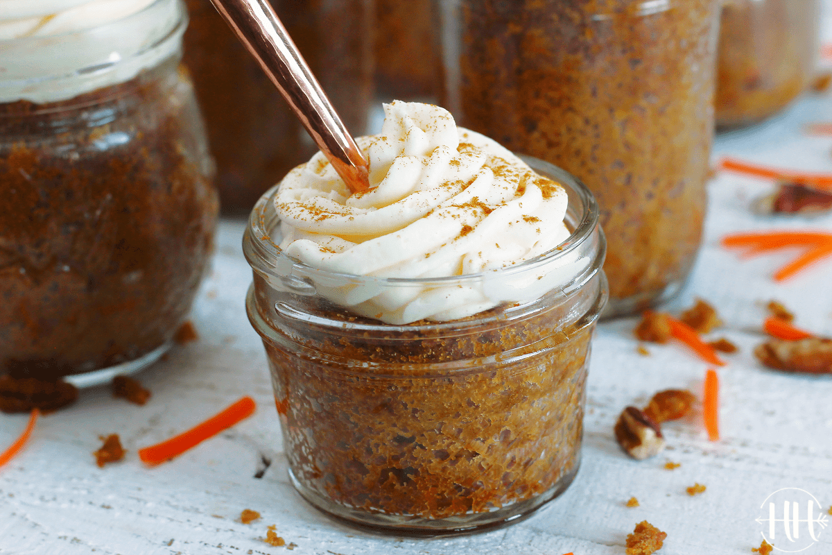 Up close photo of carrot cake in a mason jar and a copper fork in it. 