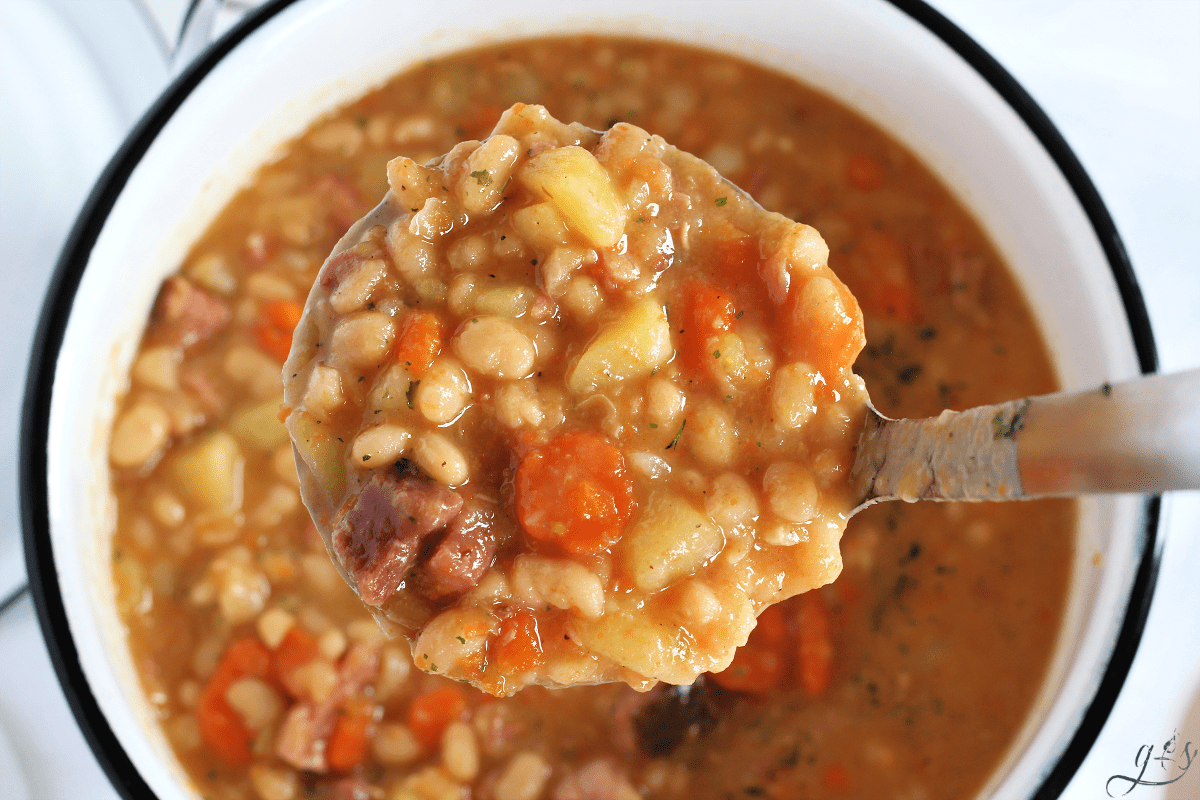 Instant Pot Ham & Bean Soup in a ladle with carrots, white beans, and potatoes.