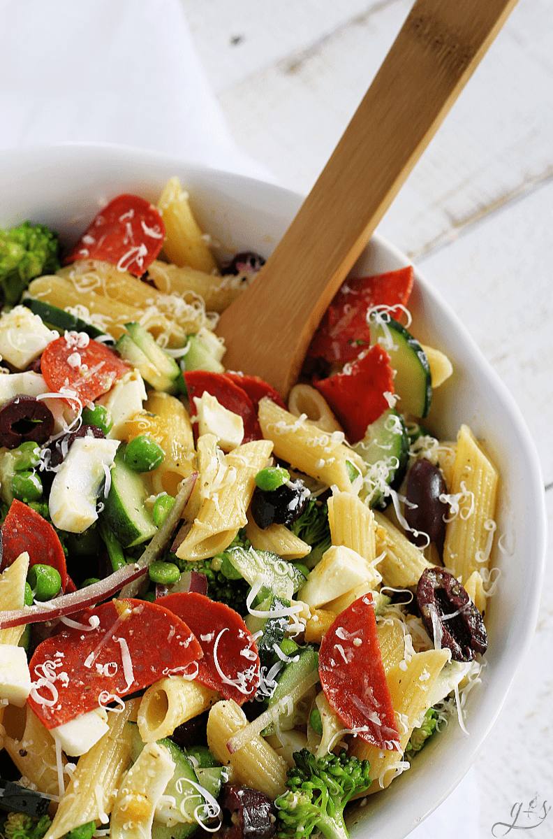 A pretty white bowl with a wooden spoon serving a cold salad with protein, fiber, and healthy fats.