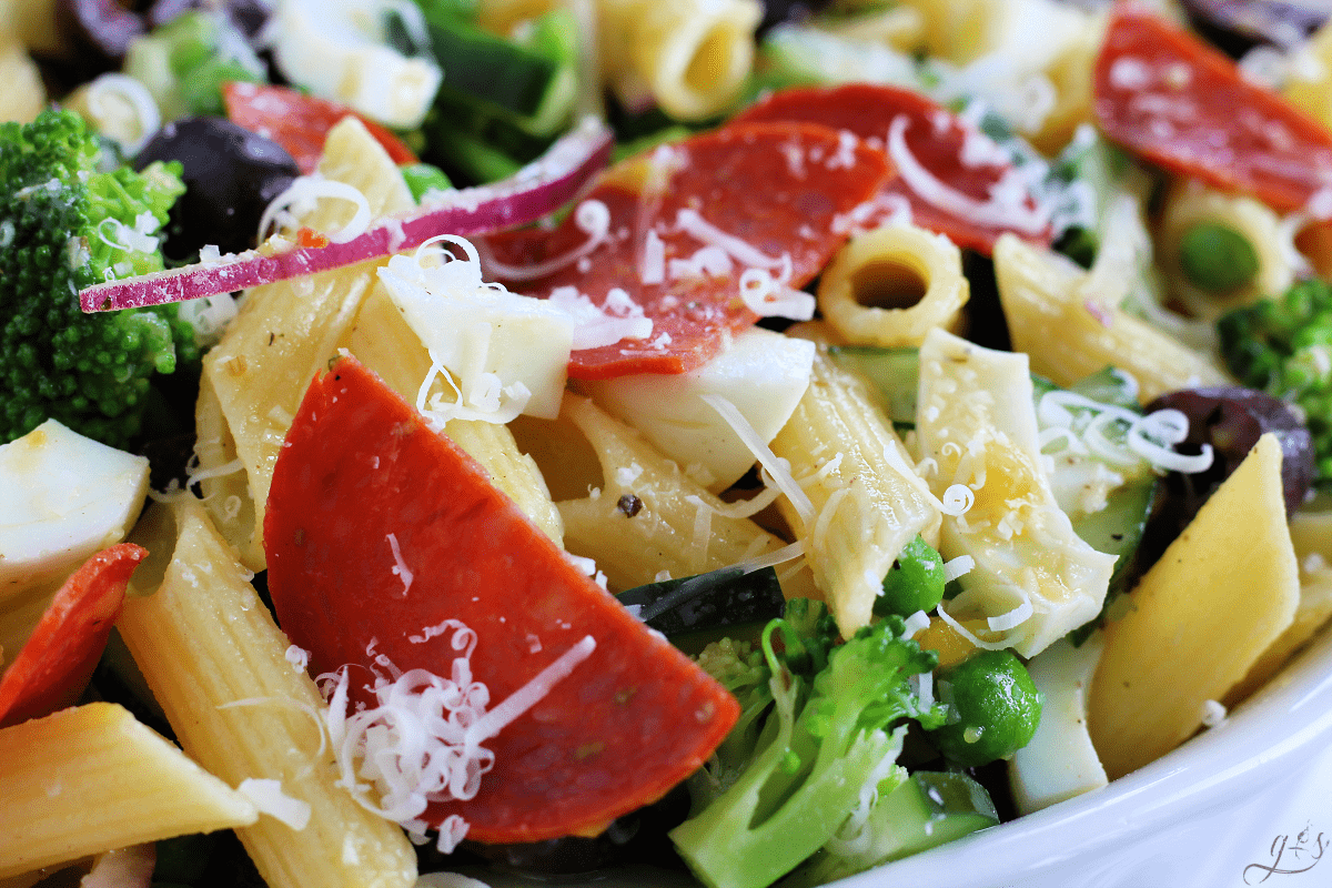 A close up shot of a delicious cold pasta salad with chopped vegetables, freshly grated Parmesan cheese, turkey pepperoni, and hard boiled eggs. 