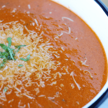 Bowl of creamy tomato soup topped with Parmesan cheese and julienned basil.