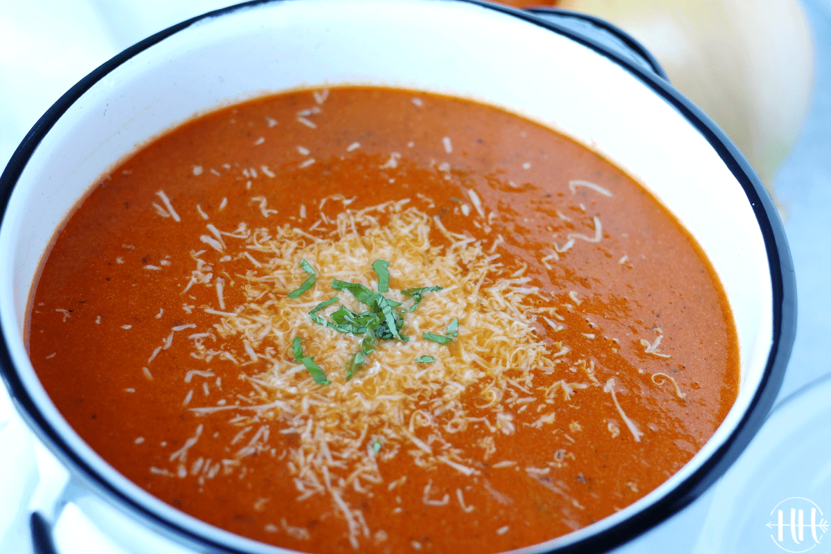 Beautiful photo of a large pot of a tomato soup recipe topped with cheese and basil.