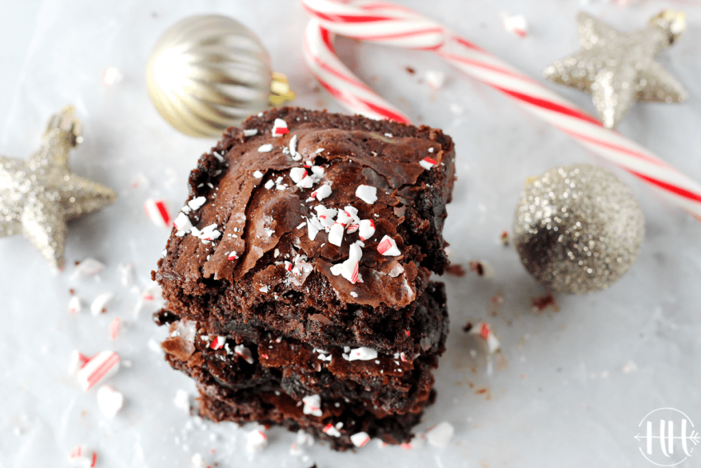 3 peppermint essential oil brownies stacked on top of each other with candy canes and Christmas decorations around them.