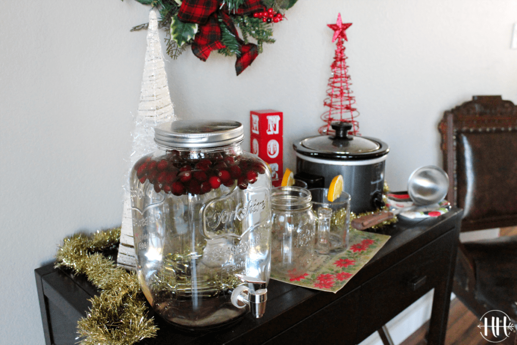 Cranberry infused water and small crockpot of apple cider on a dark wood side table.