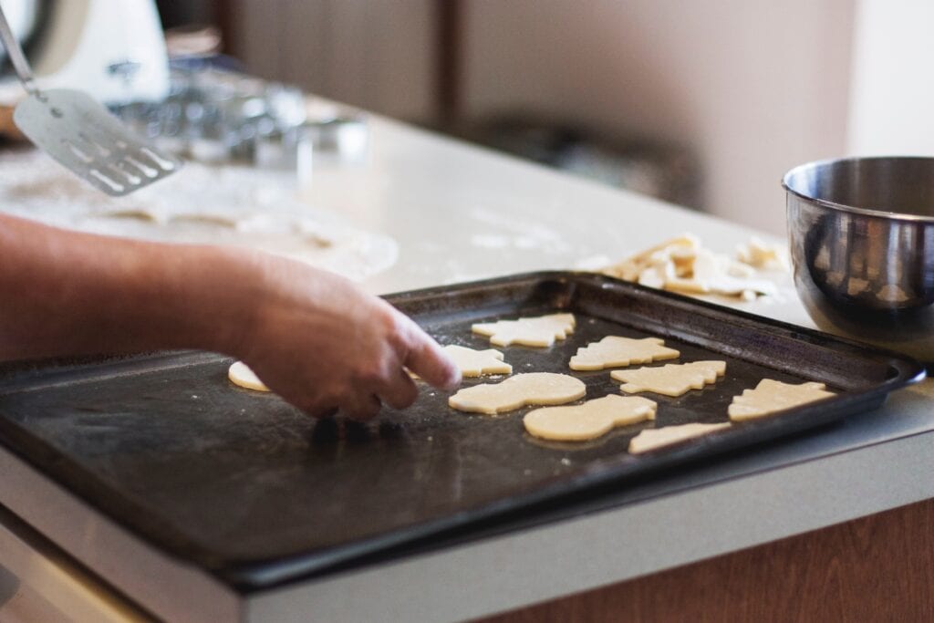 A bakers hand placing holiday sugar cookie dough on a baking sheet.