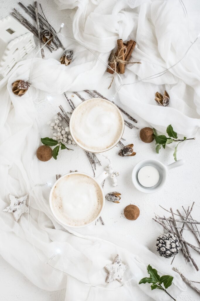 Two mugs of hot cocoa on white linens with sticks and white berries.