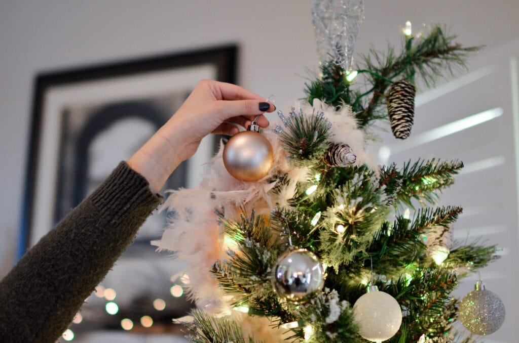 Woman's hand placing ornaments on top of Christmas tree.