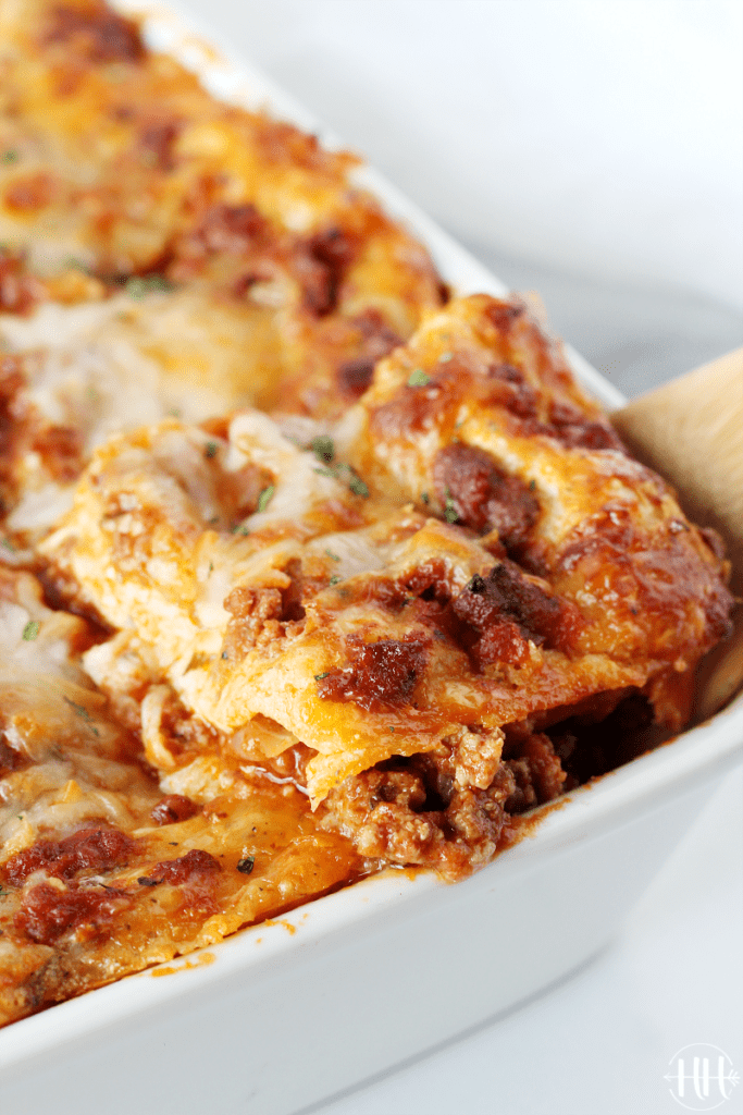 Large pan of Italian pasta noodles, ground meat, and melted mozzarella cheese showing the corner piece on a spatula.