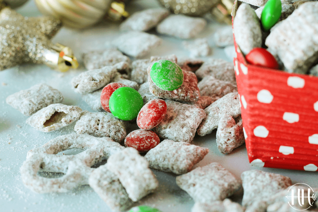 Holiday Muddy Buddy Mix with red and green candy coated chocolates scattered on a white surface.