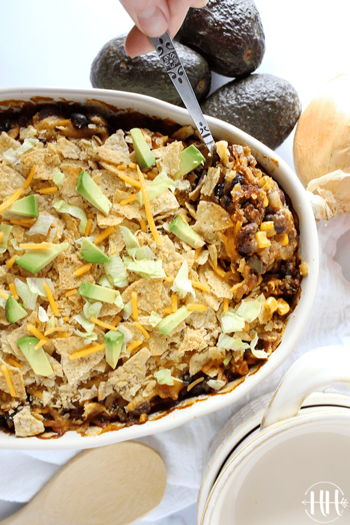 Colorful Mexican beef bake with corn and black beans topped with chips and avocado.