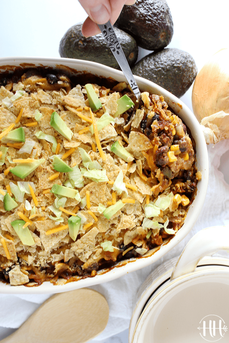 Overhead photo of ground beef enchilada casserole in a beige dish with a spoon.