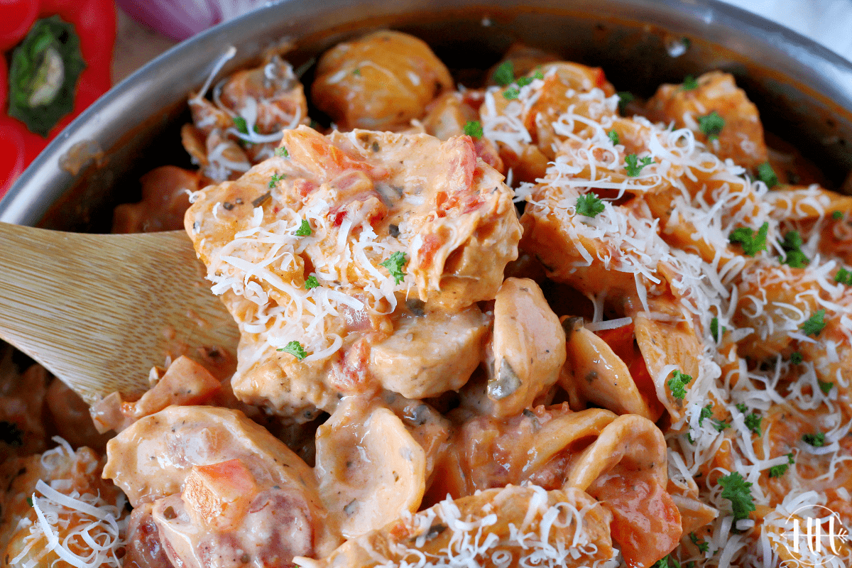 A wooden spoon getting a spoonful of chicken orecchiette with rosa sauce.