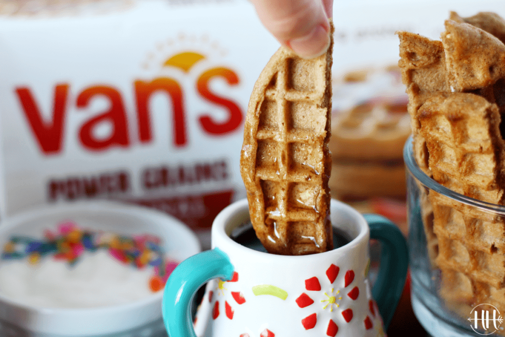 A waffle stick dipped into a small container of maple syrup. 