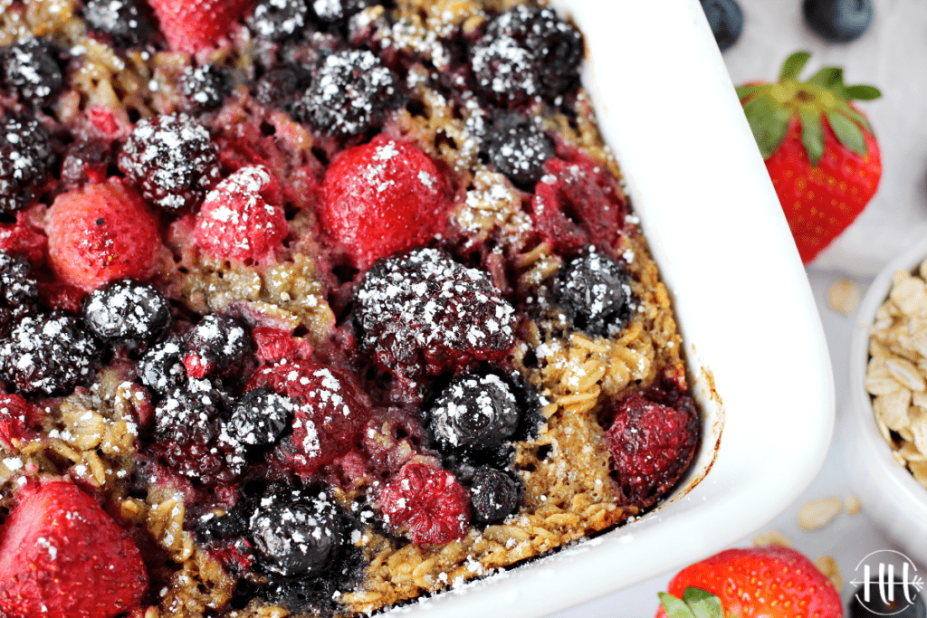 A white ceramic dish with baked berry oatmeal sprinkled with powdered sugar.