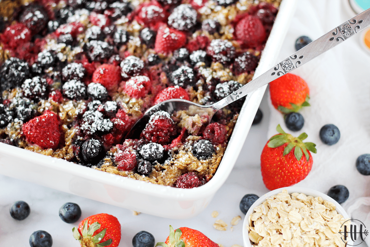 Easy Berry Baked Oatmeal - Gluten and Dairy Free recipe in a white dish surrounded by fresh berries. 