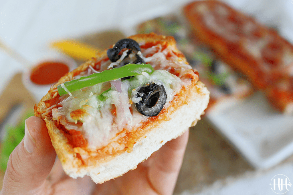 Up close shot of a slice of bread pizza with green pepper, olives, and onion. 