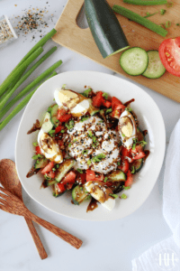 Overhead photo of a white bowl filled with sliced cucumbers, tomatoes, and hard boiled eggs.