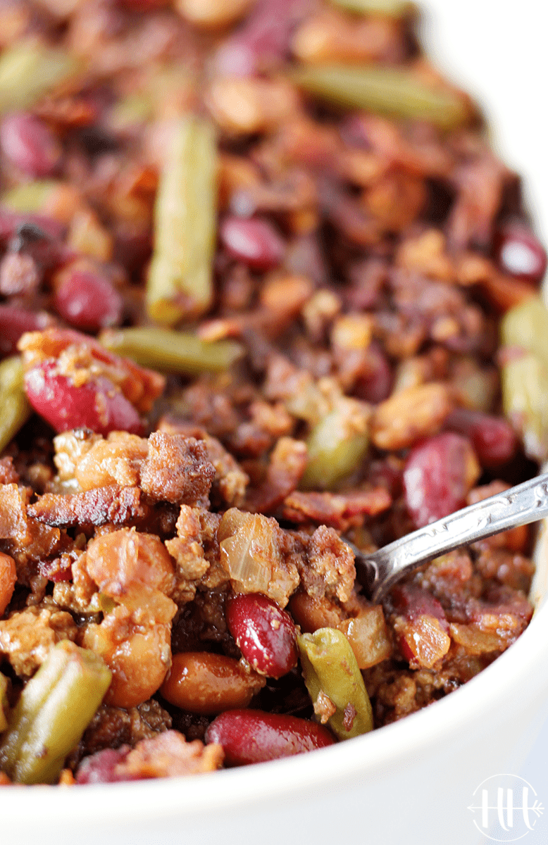 Side shot of a spoon in a pan of baked ground beef and cowboy beans.