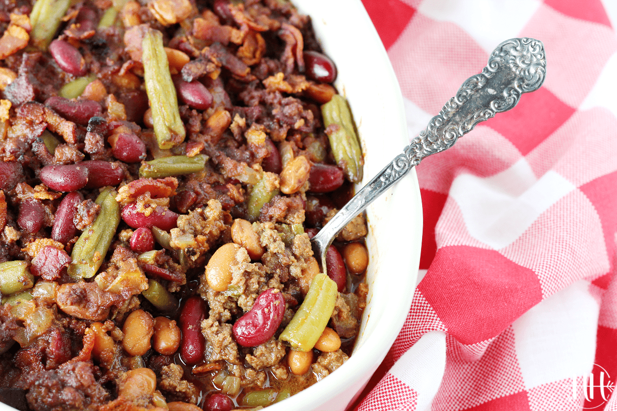 Oven baked calico beans with ground beef in a white ceramic dish with a spoon.