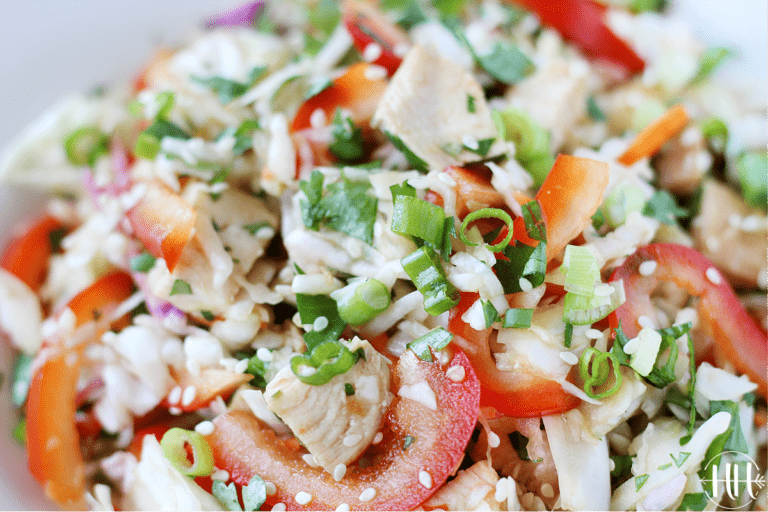 Sliced green onions and white sesame seeds on top of Asian-inspired chicken slaw salad.