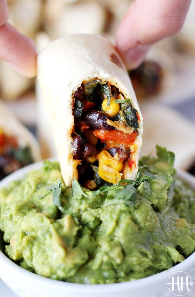 Up close photograph of a vegetarian southwest egg roll recipe baked in the air fryer being dipped in homemade guacamole.