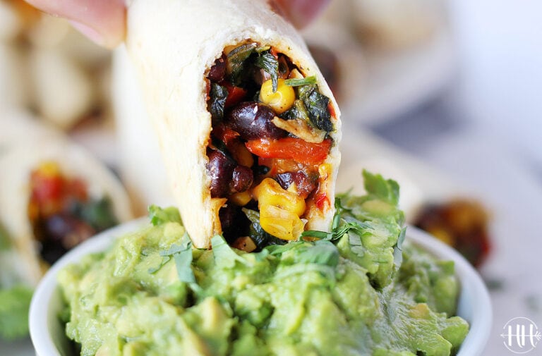 Up close photo of a vegan southwest egg roll with black beans dipped into guacamole.