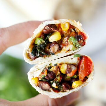 A woman's hands holding two halves of southwest egg rolls filled with black beans.