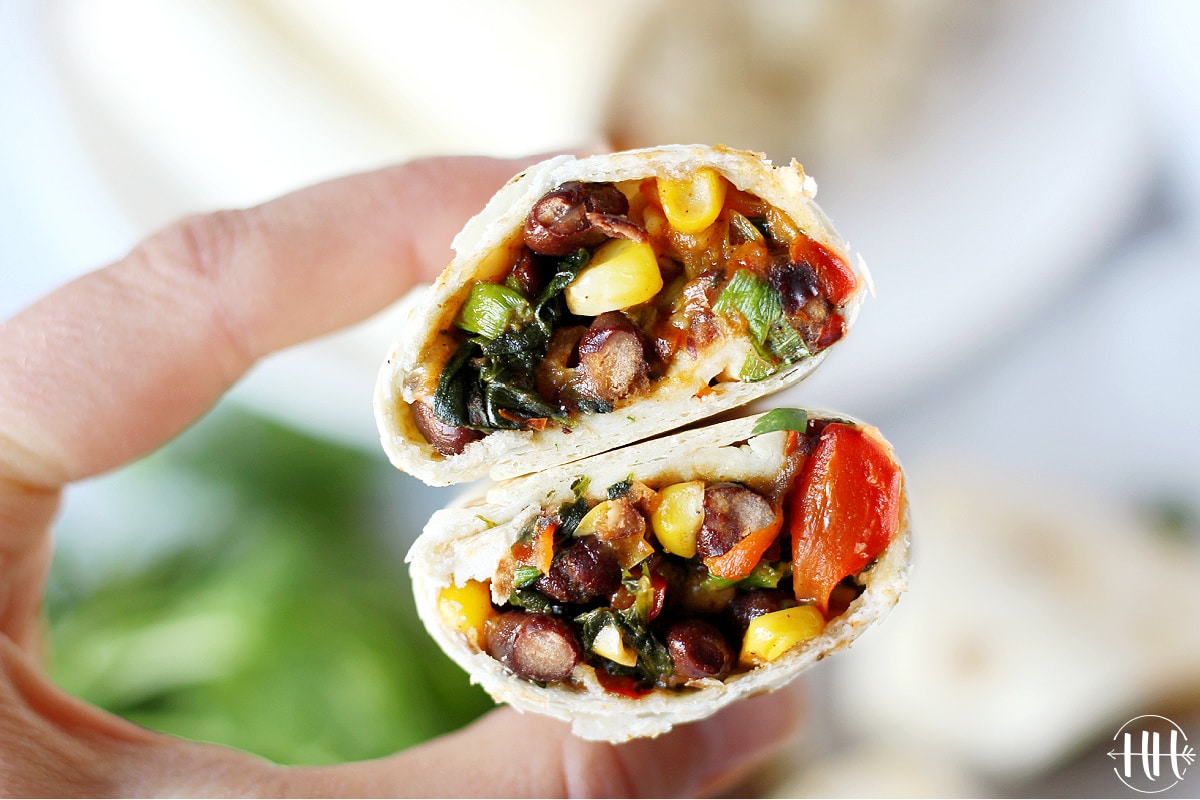 A woman's hands holding two halves of southwest egg rolls filled with black beans.