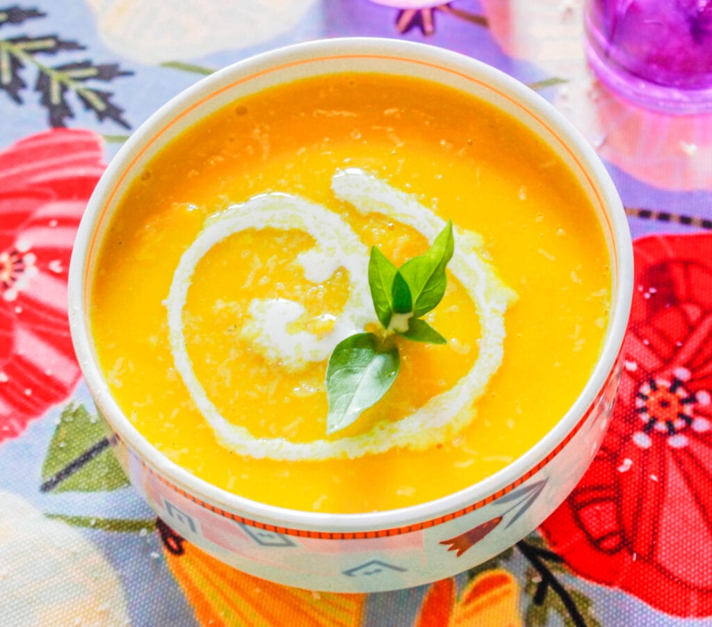 Easy Butternut Squash Soup recipe is bright and creamy with a swirl of cream and topped with fresh basil leaves. 
