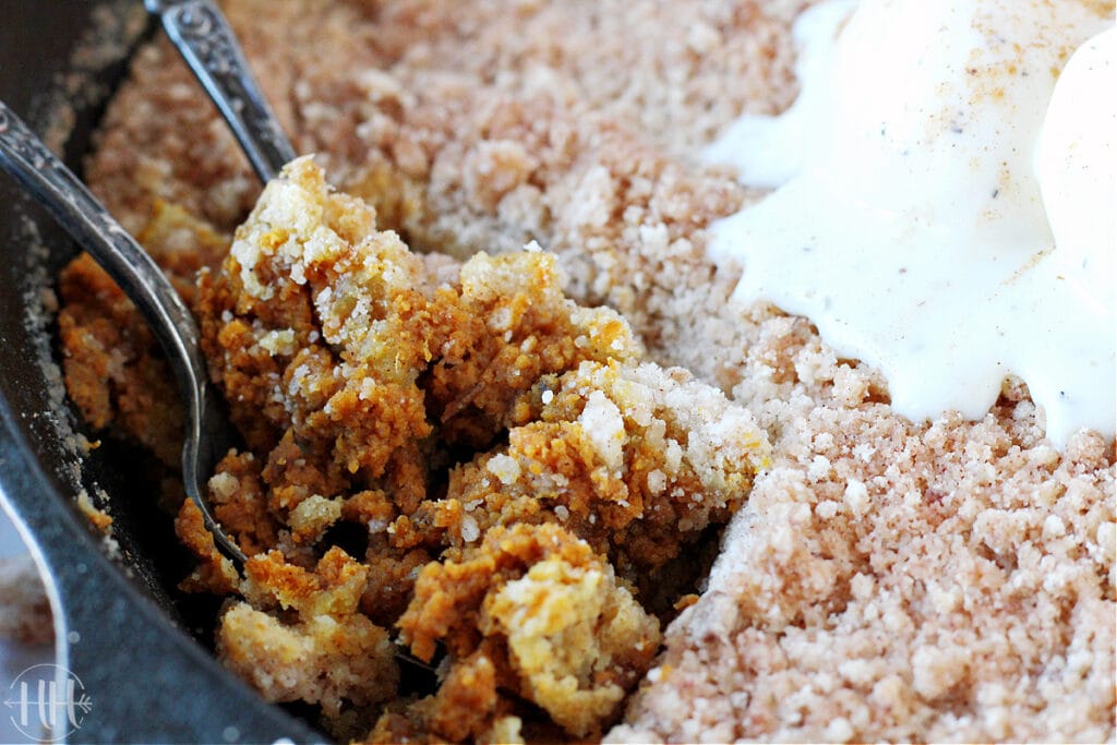 Two spoons digging into a pumpkin crisp in a cast iron skillet.