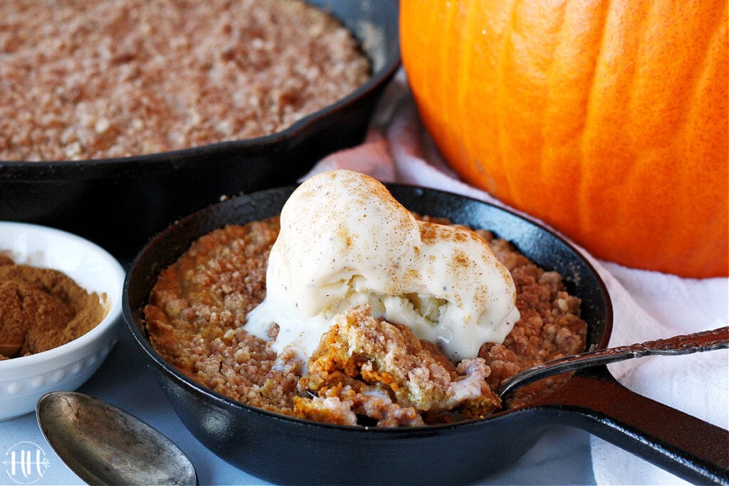 A small cast iron skillet filled with gluten free pumpkin crumble topped with vanilla ice cream. 