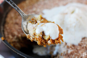 A spoon with melting ice cream on top of pumpkin pie crisp.