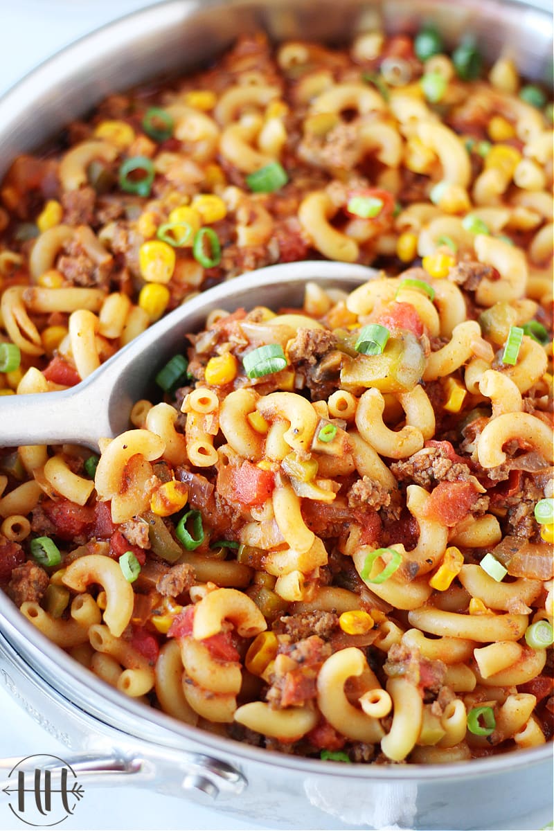 A large spoon digging into a pan of healthy goulash with vegetables.