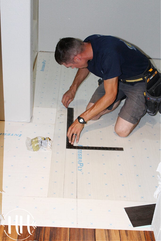 A contractor drawing a straight line with pencil on a subfloor.