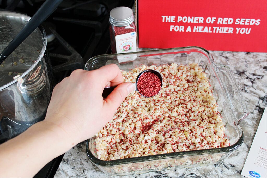 A pan of puffed rice cereal treats sprinkled with cranberry seeds.