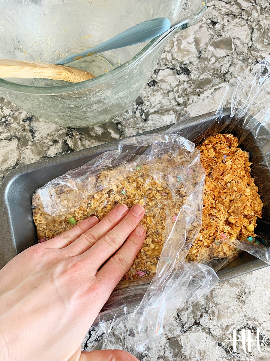 A woman's hand pressing no bake Easter M&M Bars batter into a bread pan.