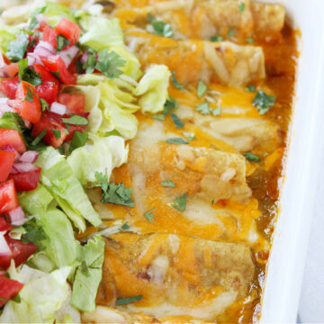 Up close photo of easy beef enchiladas in a white pan topped with lettuce.