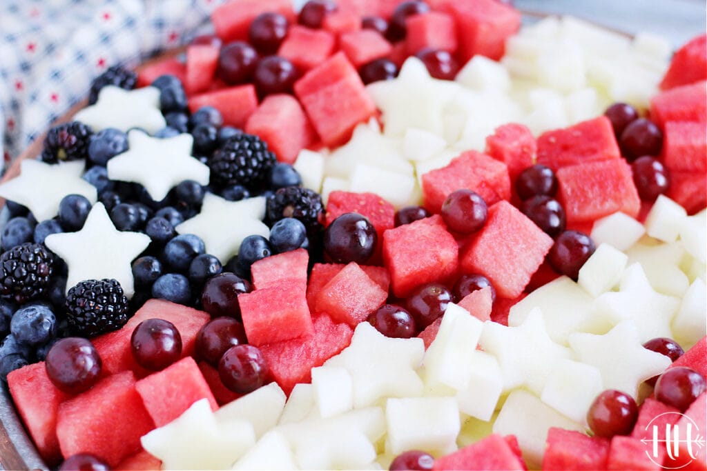 Up close photo of watermelon pieces, white canary melon stars, blueberries, and blackberries in a flag pattern. 