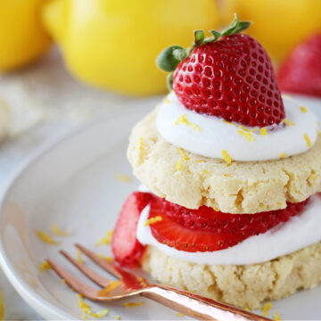 Up close photo of two lemon shortbread cookies with whipped cream and sliced strawberries.
