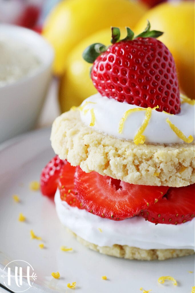 Up close side view of lemon cookies with whipped cream and strawberries sandwiched between them.