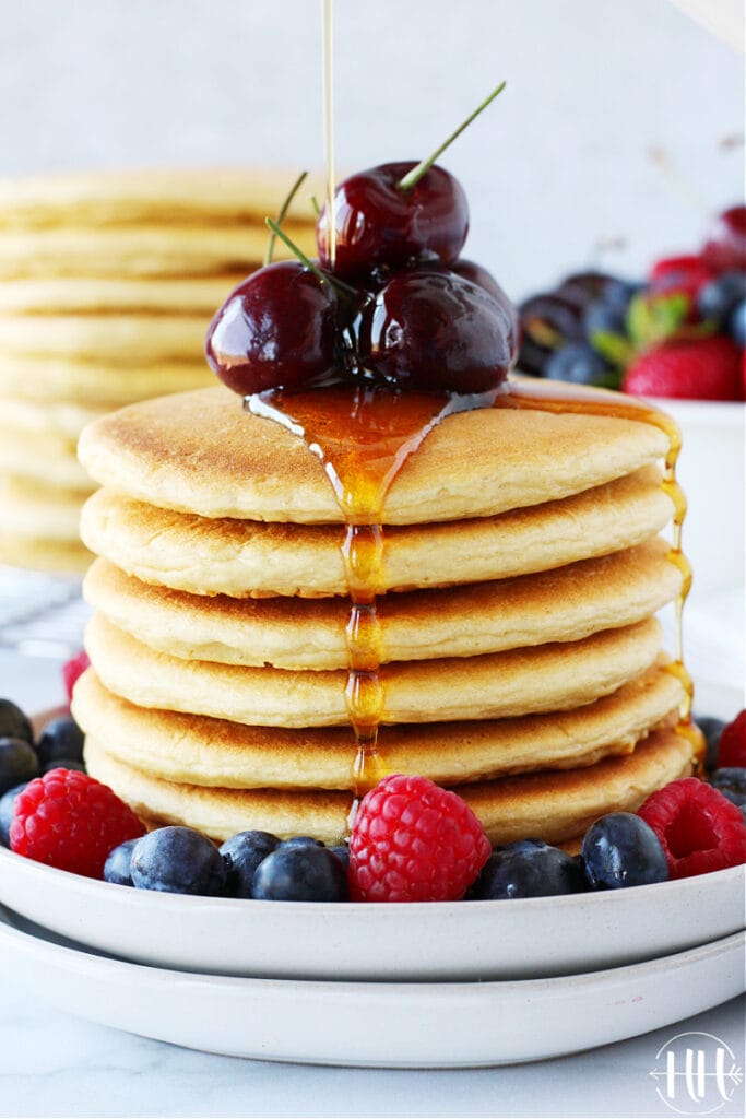 Delicious stack of protein pancakes with fresh cherries and syrup cascading over the side.